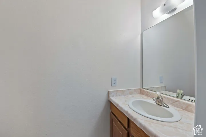Vanity featuring a wood-finish cabinet, patterned laminate countertop, integrated oval sink, chrome-finish faucet, and an oversized wall-mounted mirror with a horizontal light fixture