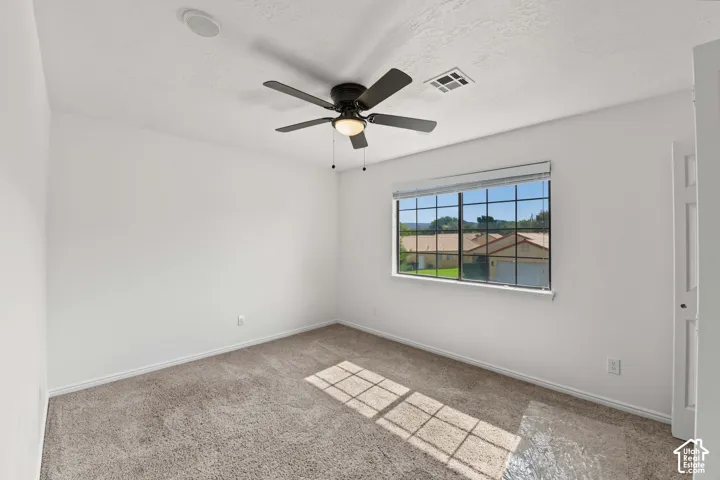 Neutral wall finishes, plush carpeting, ceiling fan with integrated lighting, and a multi-pane window with horizontal blinds