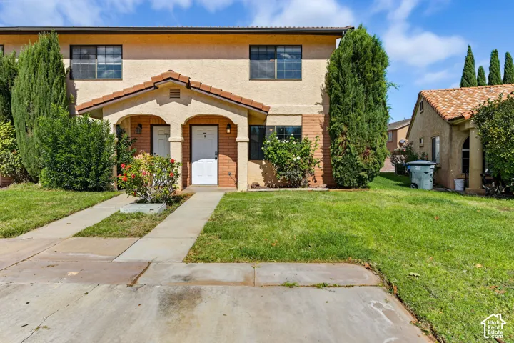 Stucco exterior featuring a dual-entry covered porch, concrete walkways, tiled roof, and mature landscaping