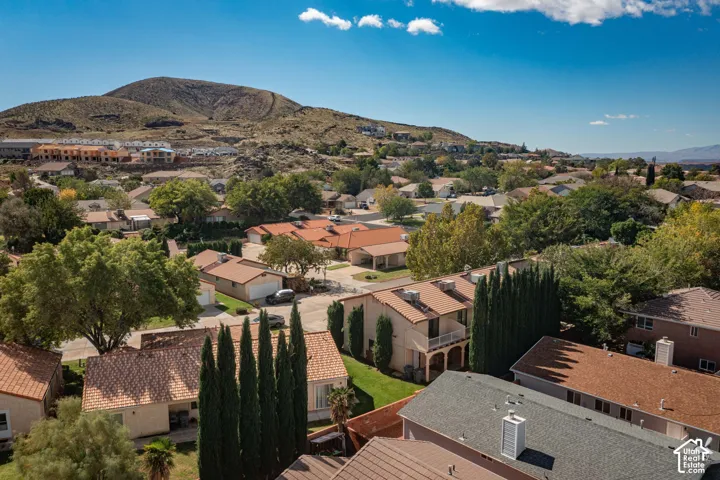 Aerial perspective featuring terracotta-style roof tiles, stucco siding, mature evergreen trees, and a mountain backdrop