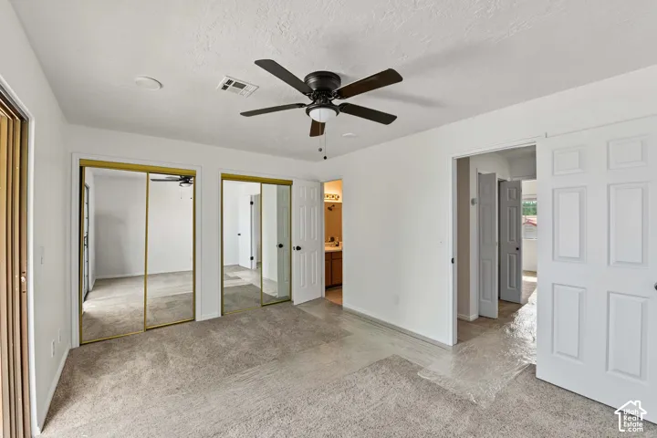 Interior space featuring neutral carpeting, dual mirrored closet doors with gold-tone frames, and a multi-blade ceiling fan with an integrated light fixture