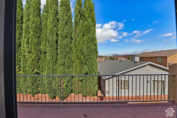 Balcony featuring a metal railing, tile flooring, and a backdrop of mature Italian cypress trees