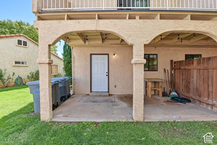 Covered patio with arched stucco columns, concrete flooring, exterior wall-mounted lighting, and wood privacy fencing