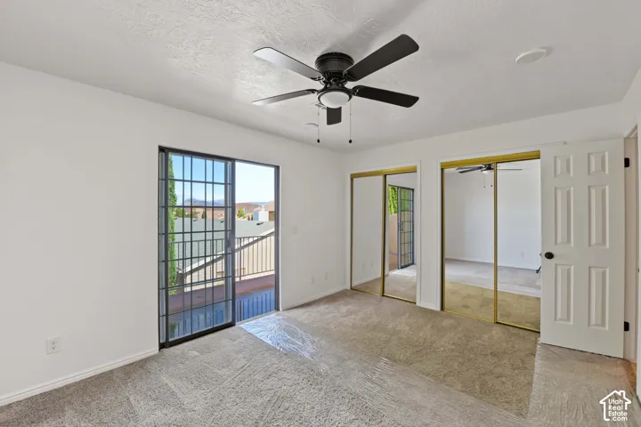 Room featuring carpeting, a ceiling fan with integrated lighting, dual sliding glass door access to a balcony, and double closets with mirrored doors