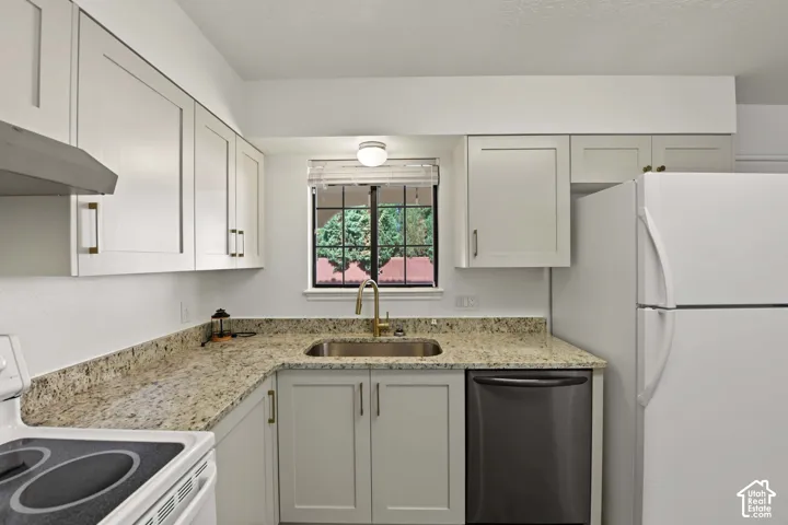 Kitchen featuring light-toned cabinetry, stone-finish countertops, stainless steel sink with a brass-finish faucet, and built-in appliances