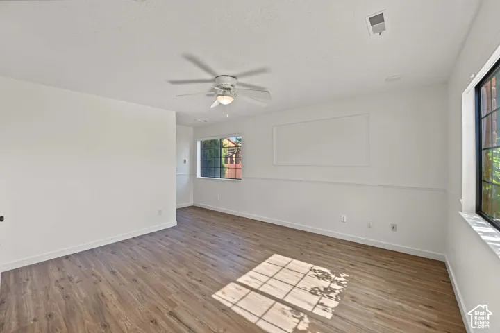 Interior space featuring wood-finish flooring, white walls with chair rail molding, multi-pane windows, and a central ceiling fan with an integrated light fixture