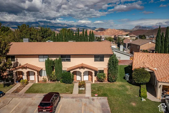 Stucco exterior featuring dual-pitched tile roofing, covered entryways with arched architectural detailing, and mountain backdrop