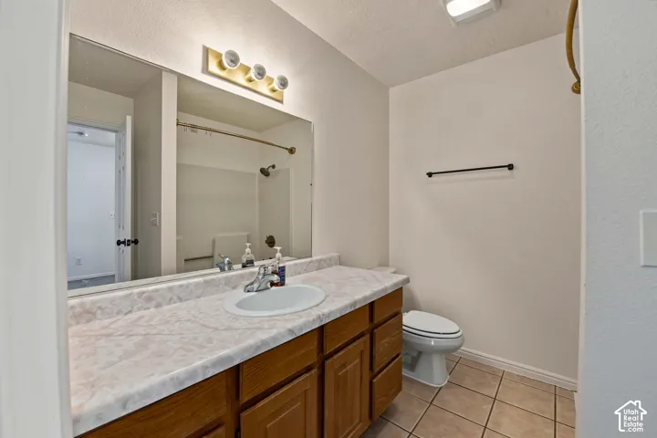 Bathroom featuring a wood vanity with a stone-finish countertop, integrated oval sink, full-width mirror, and ceramic tile flooring