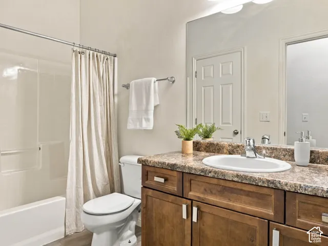 Bathroom featuring a wood-finish vanity, stone-pattern countertop with integrated oval sink, chrome faucet hardware, and a white tub-shower combination with a full-width wall mirror