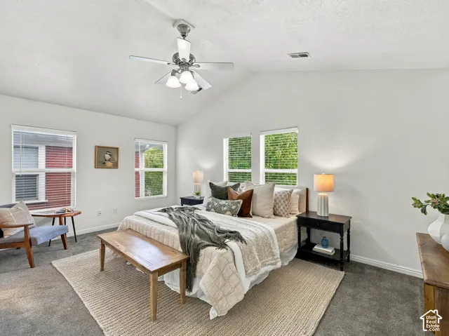 Vaulted ceiling with a central brushed-nickel ceiling fan and multi-light fixture, accompanied by four windows with horizontal blinds and neutral carpeting