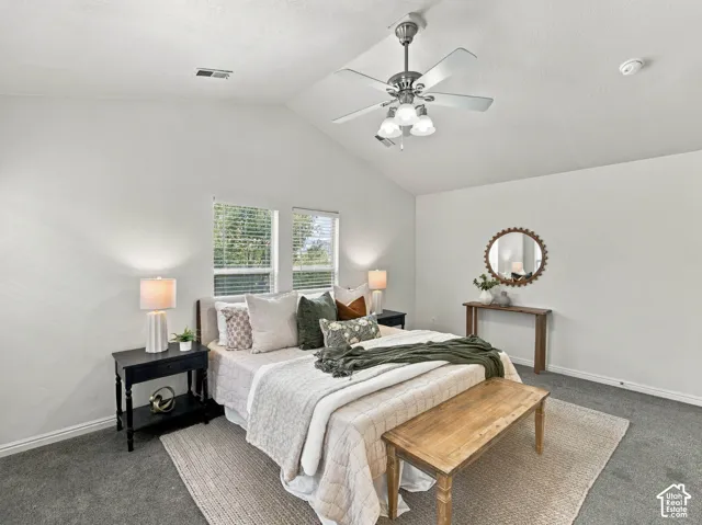 Vaulted ceiling featuring a central brushed-nickel ceiling fan with integrated lighting, dual windows with blinds, and neutral carpeting