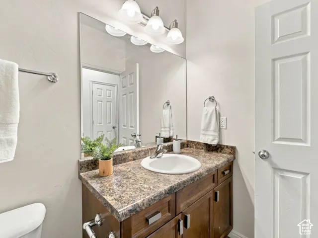 Vanity with wood-finish cabinetry, stone-patterned countertop, integrated undermount sink, multi-bulb wall-mounted lighting fixture, and large wall-to-wall mirror