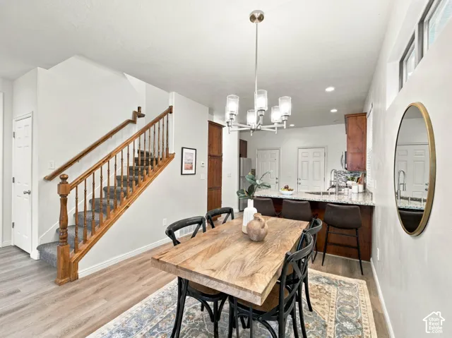 Wood-finish staircase with turned spindles, multi-light chandelier, wood-finish cabinetry, stone countertops, and wood-finish flooring