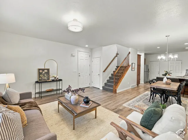 Open-concept floor plan featuring wood-finish flooring, a staircase with a wooden handrail and balusters, a multi-paneled entry door, and multi-light hanging fixtures