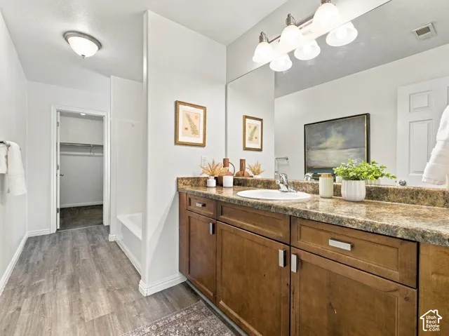 Bathroom featuring a wood-finish vanity with a stone-composite countertop, an integrated sink, a full-width vanity mirror, and wood-finish flooring