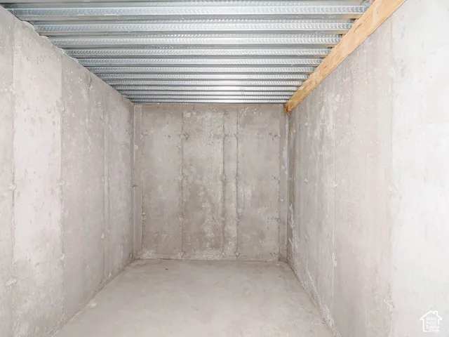 Unfinished utility space featuring poured concrete walls, a smooth concrete floor, and exposed corrugated metal ceiling panels