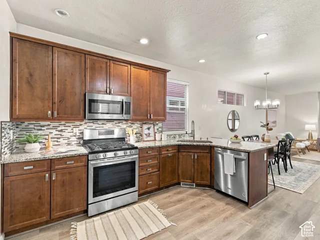 Kitchen featuring stained wood cabinetry, stone-finish countertops, stainless steel appliances, a multi-tonal tile backsplash, and wood-finish flooring