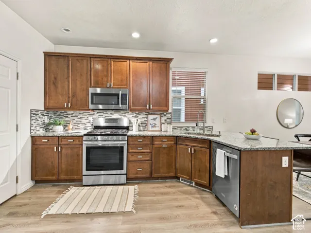 Kitchen featuring wood cabinetry, stone countertops, stainless steel appliances, a multi-tonal tile backsplash, and wood-finish flooring
