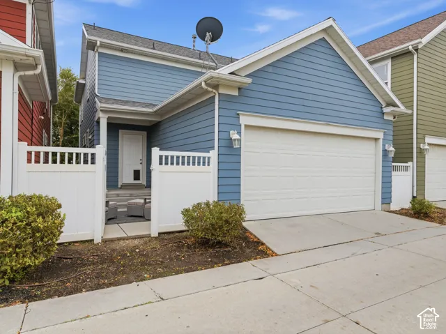 Exterior facade featuring blue horizontal siding, white trim, an attached two-car garage, and a gated entry leading to a concrete patio