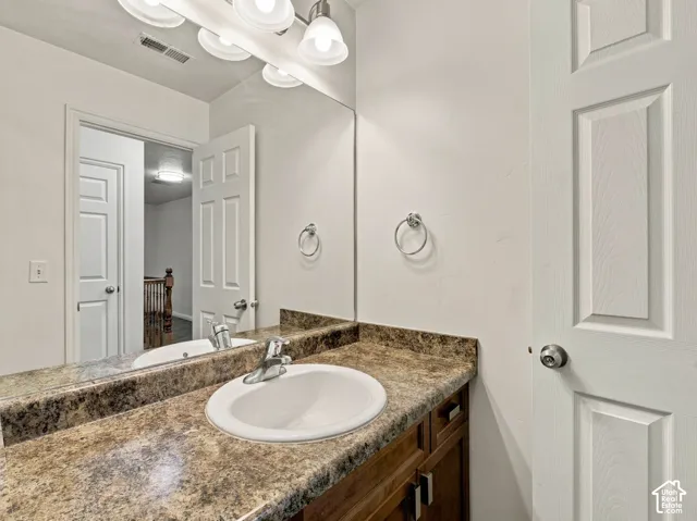 Bathroom vanity featuring a stone-patterned countertop, drop-in basin sink, chrome faucet, wood-finish cabinetry, and a full-width wall mirror