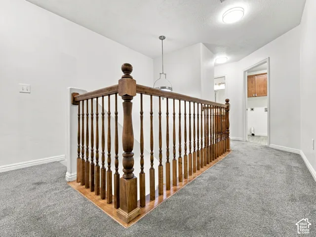 Staircase featuring a wood banister with turned balusters, grey wall-to-wall carpeting, and a polished metal pendant light fixture