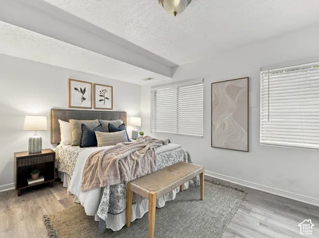 Room featuring wood-finish flooring, two windows with horizontal blinds, and a semi-flush mount ceiling light fixture