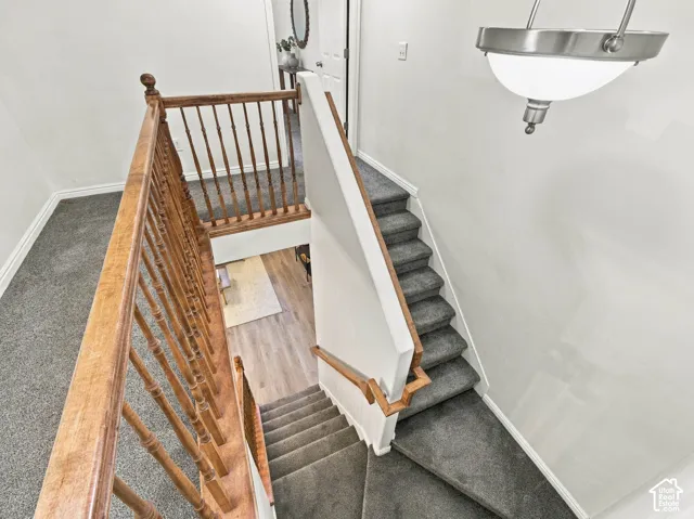 Staircase featuring wood railings with turned spindles, charcoal carpeting, and a brushed metal bowl-style pendant light fixture