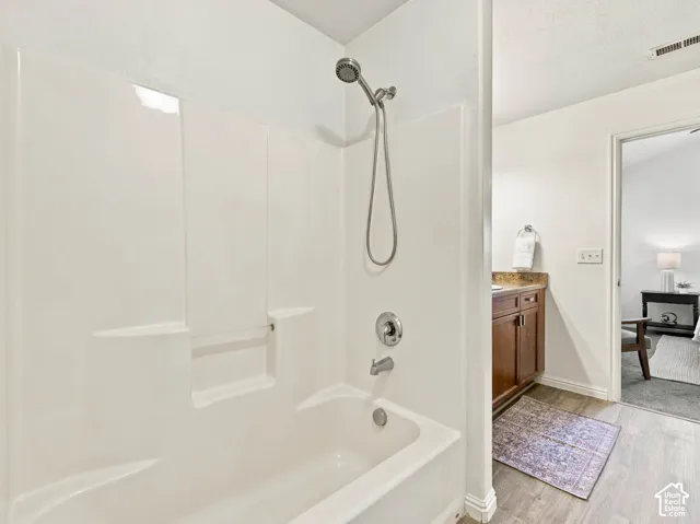 Bathroom featuring a white tub-shower enclosure with a handheld showerhead, wood-finish cabinetry, and wood-finish flooring