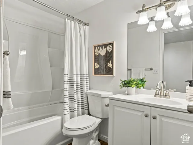 Bathroom featuring a white vanity cabinet with a solid surface countertop, an oval undermount sink, a multi-light fixture, and a white one-piece shower and tub surround