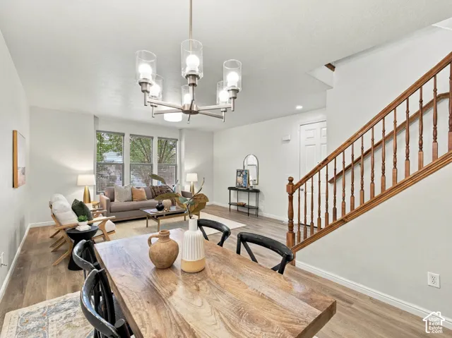 Open-concept space featuring wood-finish flooring, a multi-arm chandelier with cylindrical glass shades, and a staircase with a stained-wood handrail and balusters