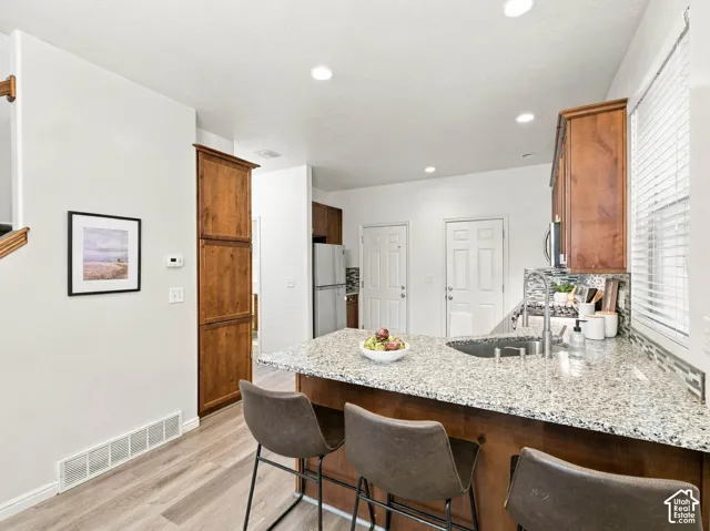 Kitchen featuring stone countertops, wood-finish cabinetry, wood-finish flooring, recessed lighting, and a dual-basin stainless steel sink