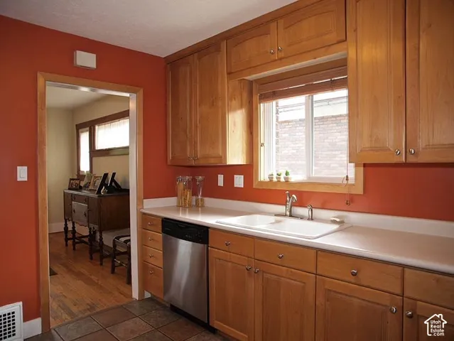 Kitchen featuring shaker-style wood cabinetry, solid-surface countertops, dual-basin sink with stainless steel fixtures, and stainless steel dishwasher