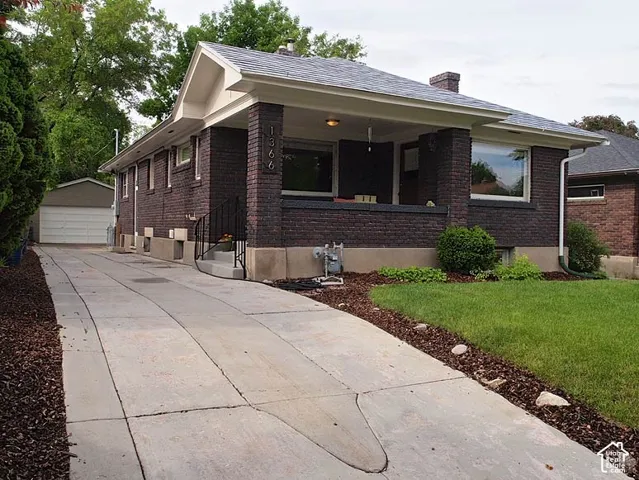 Dark brick exterior featuring a covered front porch, concrete driveway, and detached garage