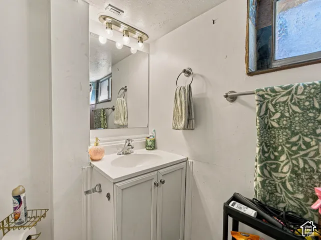 White vanity with a single-basin integrated countertop, polished chrome faucet, four-bulb vanity light fixture, and wall-mounted mirror
