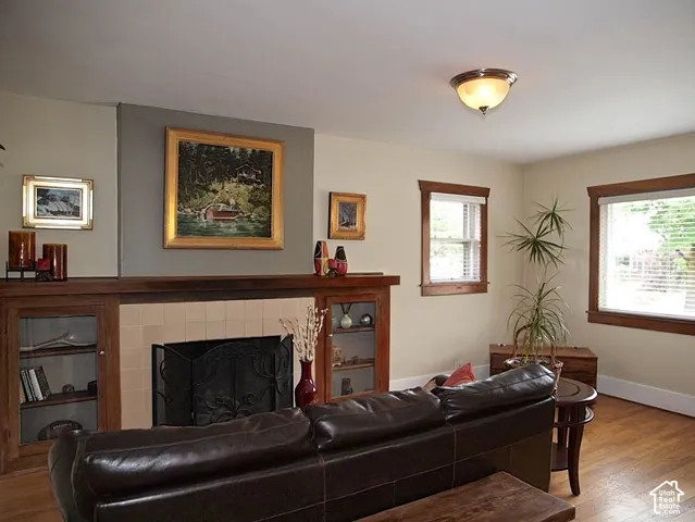 Fireplace featuring a tile surround, wood mantel, and flanking built-in glass-front cabinetry, complemented by wood-finish flooring and wood window trim