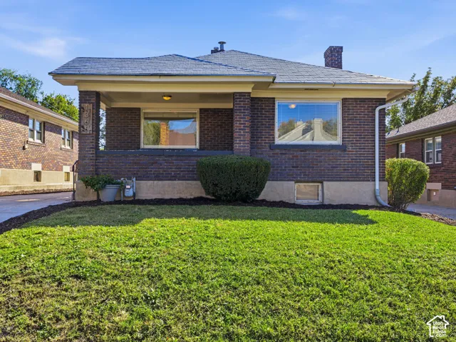 Brick exterior featuring a covered front porch, low-pitch hip roof, masonry chimney, and large pane windows