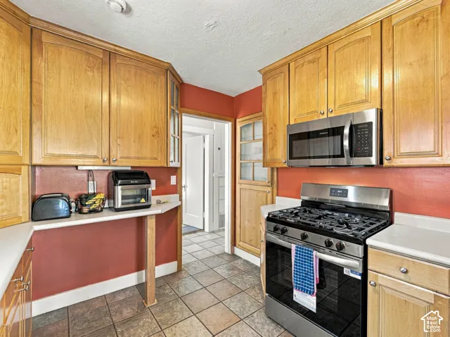 Kitchen featuring natural wood cabinetry, stone-finish tile flooring, integrated stainless steel gas range, and a built-in over-the-range microwave