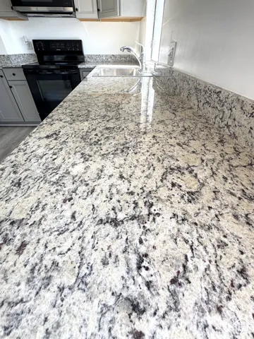 Polished stone countertops with matching backsplash, undermount stainless steel sink, chrome faucet, and gray shaker-style cabinetry