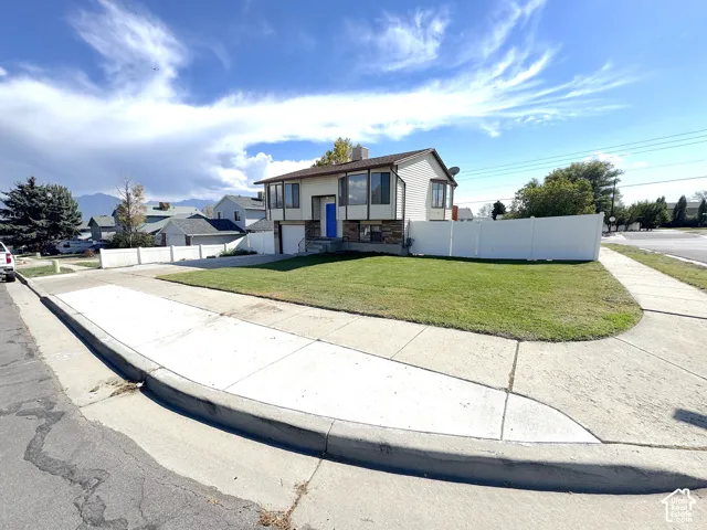 Split-level exterior featuring light-toned horizontal siding, stone masonry accents, multiple bay windows, and a privacy-fenced corner lot