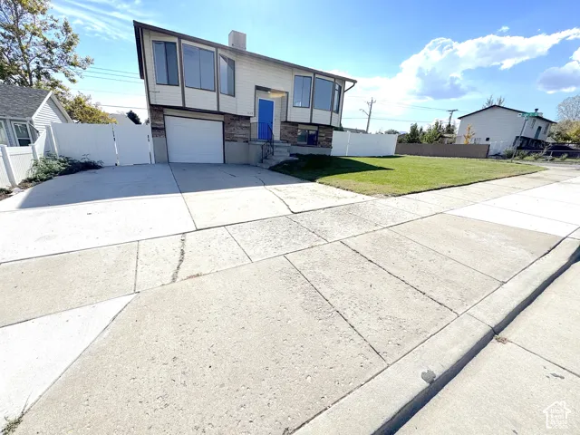 Split-level exterior featuring light-toned horizontal siding, a multi-paneled stone facade, an attached garage, and a fenced-in perimeter