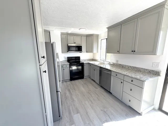 Kitchen featuring light gray shaker-style cabinetry, stone-finish countertops, stainless steel appliances, and wood-finish flooring