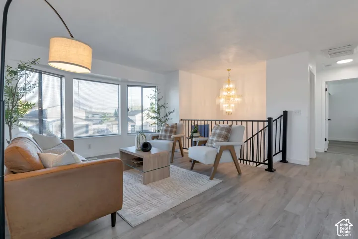 Living area featuring wood-finish flooring, large multi-pane windows, a tiered crystal chandelier, and a black metal spindle railing