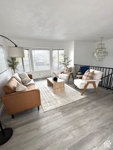 Living area featuring wood-finish flooring, a multi-panel bay window, and a tiered crystal chandelier with a matte black metal railing
