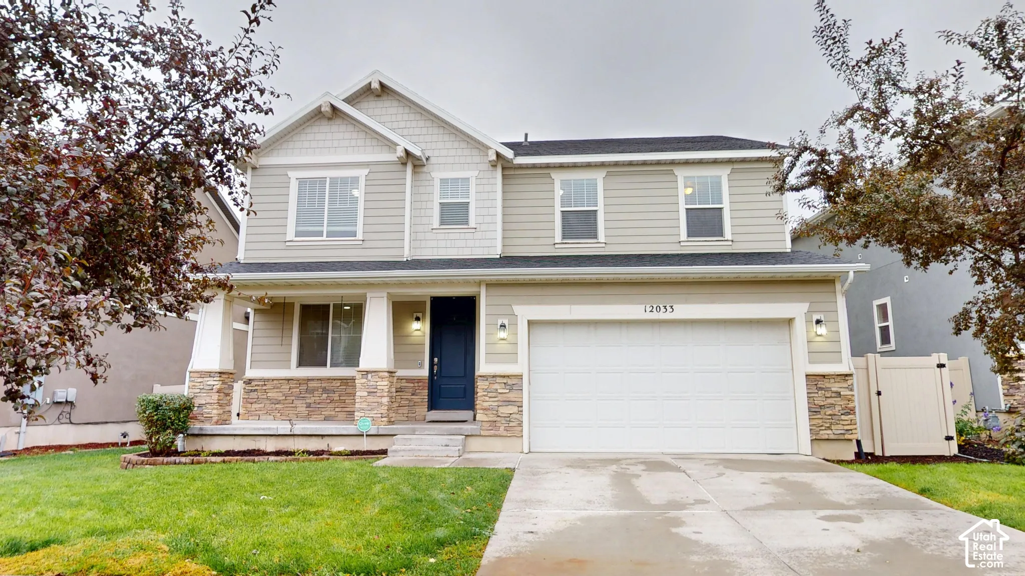Two-story exterior featuring a mix of horizontal lap and shake siding, stone veneer accents, a covered front porch with tapered columns, and a two-car garage