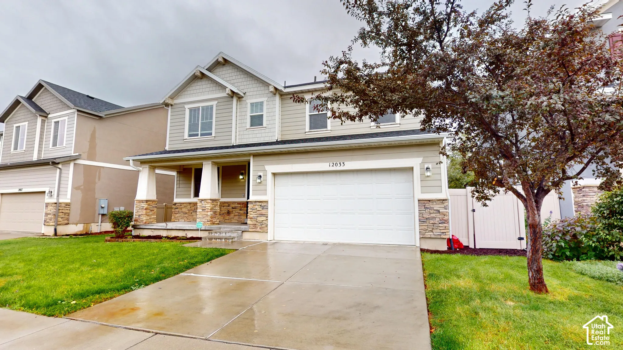 Two-story exterior featuring horizontal lap siding, shake-shingle gables, stone veneer accents, a covered front porch with tapered columns, and an attached two-car garage