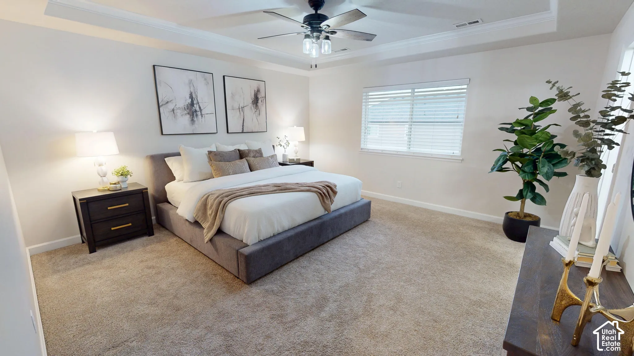 Primary suite featuring a tray ceiling with crown molding, neutral carpeting, and a ceiling fan with integrated lighting