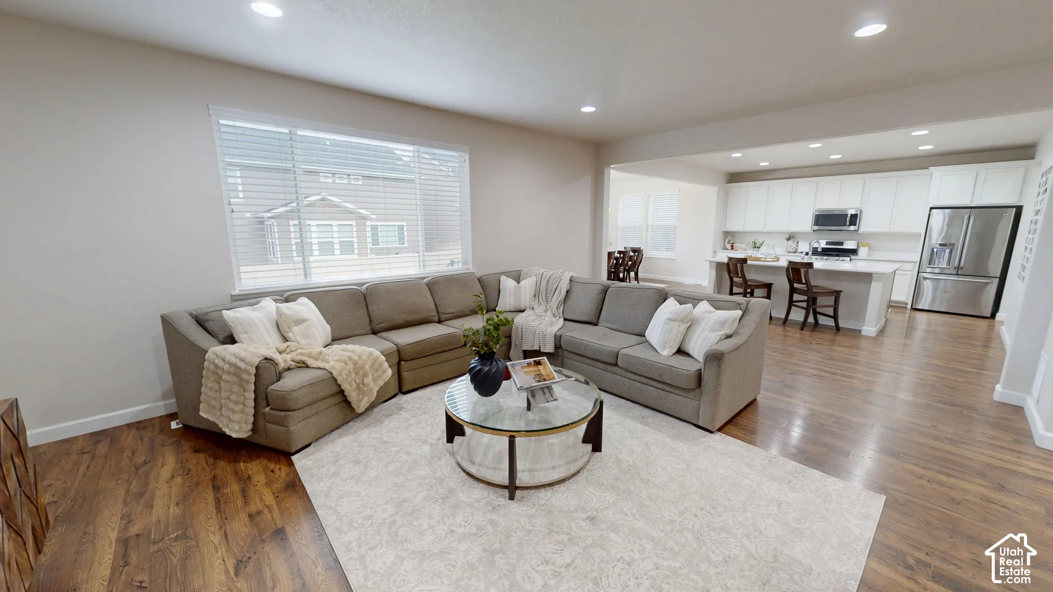 Open floor plan featuring wood-finish flooring, recessed lighting, and a kitchen equipped with white cabinetry, a center island, and stainless steel appliances