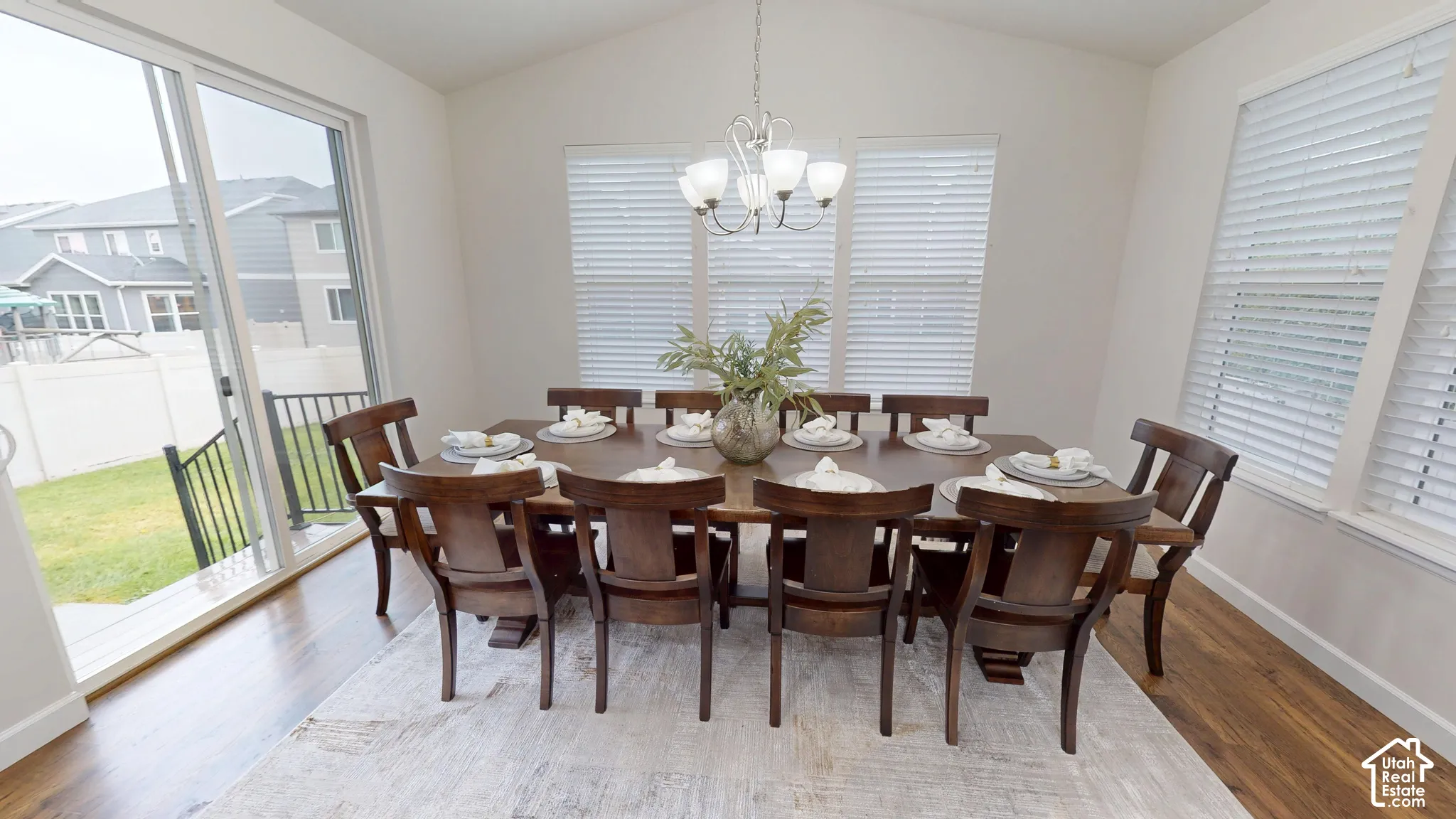 Extra large dining area featuring vaulted ceilings, wood-finish flooring, multi-pane windows with integrated blinds, and a multi-light chandelier