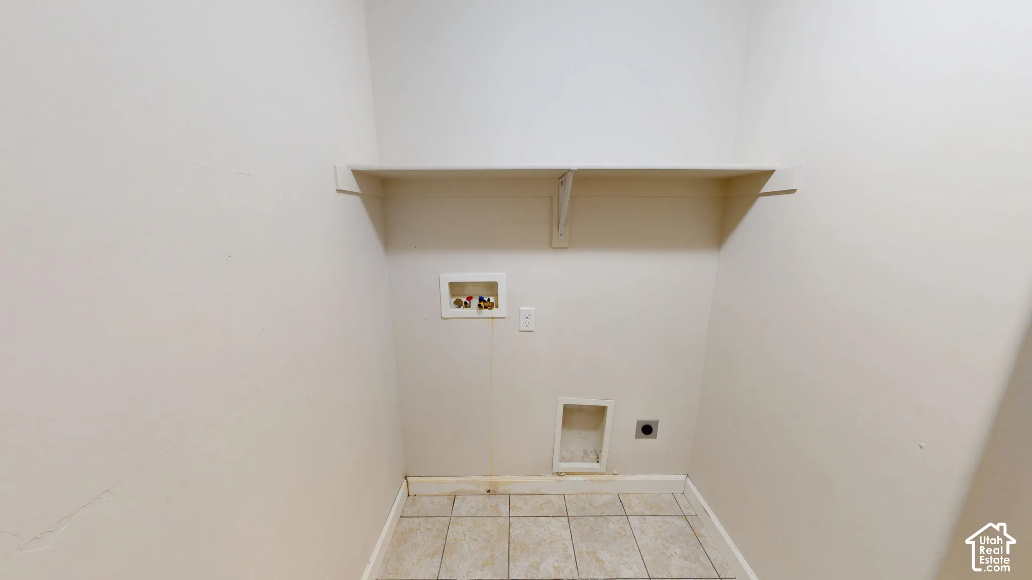 Utility area featuring tile flooring, a wall-mounted storage shelf, and dedicated water, electrical, and ventilation hookups