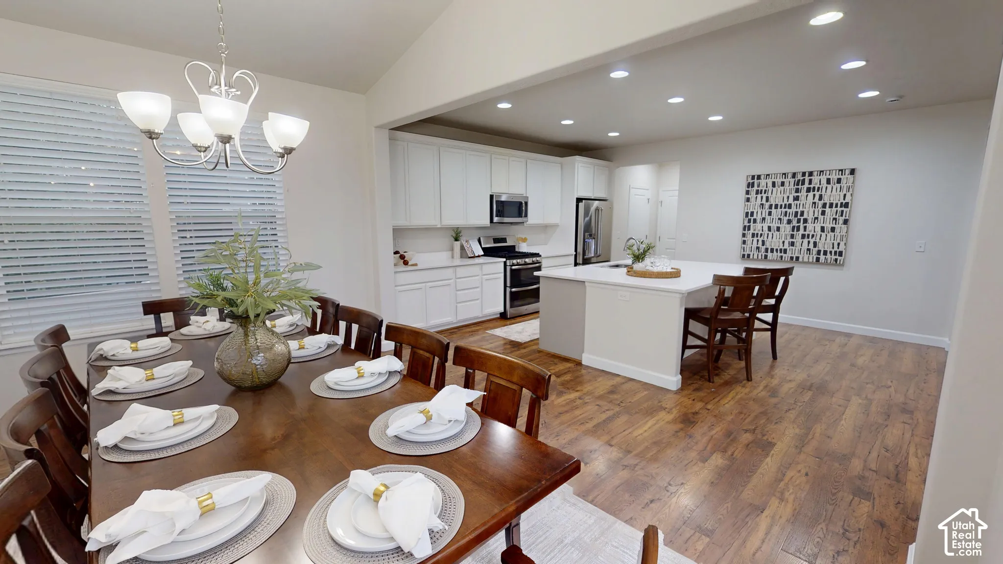 Open-concept kitchen and dining area featuring white shaker-style cabinetry, a central island with quartz countertops, stainless steel appliances, recessed lighting, and wood-finish flooring
